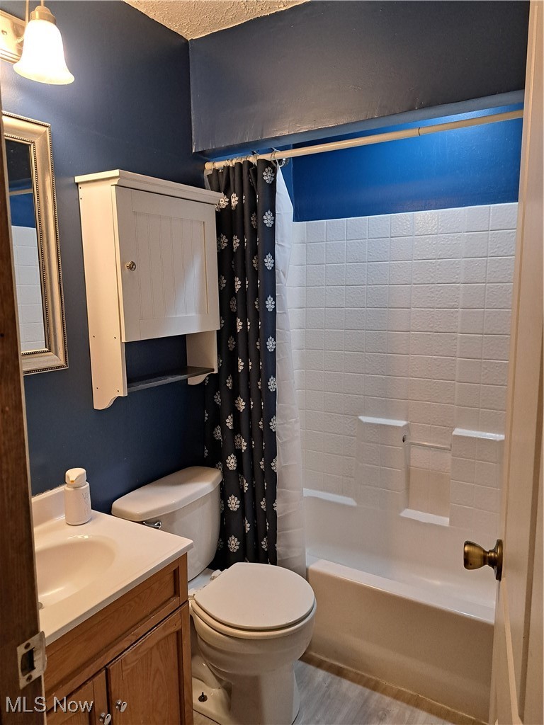 3813 State Road Vermilion, OH 44089 - Photo 28 of 28 Full bathroom featuring vanity, toilet, a textured ceiling, shower / bath combo with shower curtain, and hardwood / wood-style floors