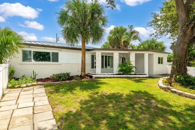 a white house with a large pool yard and palm trees