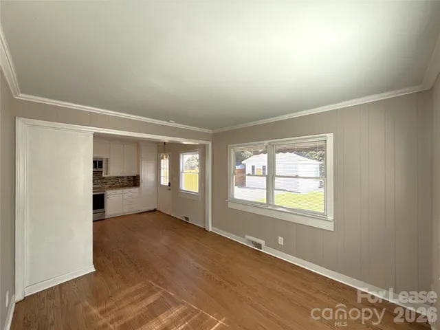 an empty room with windows and view of kitchen