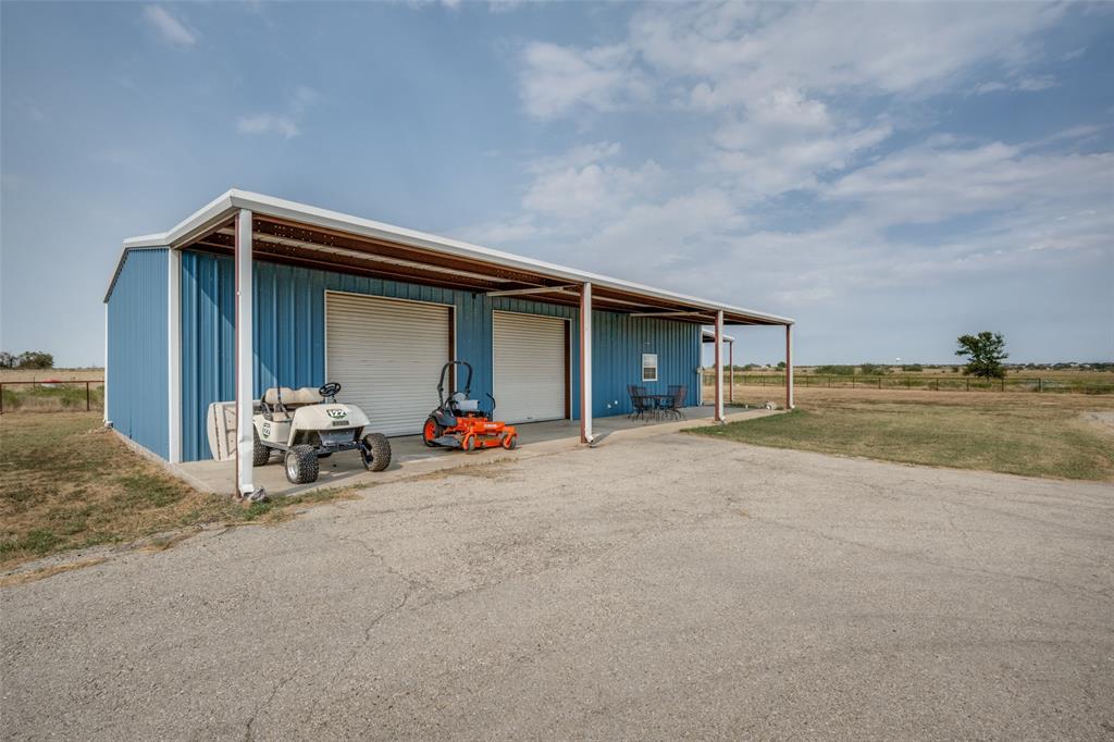 8400 Holder Road Northlake, TX 76247 - Photo 27 of 36 Barndo -Blue metal building with two garage doors, an extended covered porch, a concrete driveway, and an expansive open landscape