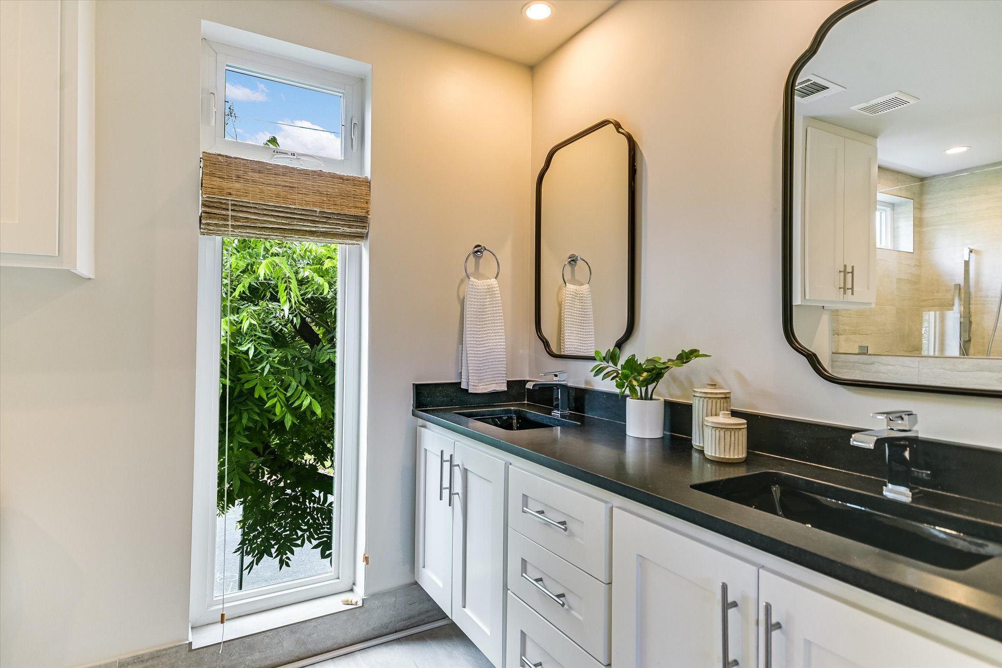 1605 Hether Street Austin, TX 78704 - Photo 16 of 26 Double vanity featuring black countertops and undermount sinks, white cabinetry with silver hardware, and dual framed mirrors