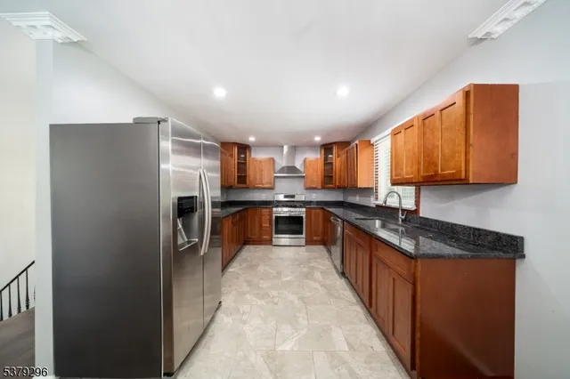 a large kitchen with stainless steel appliances granite countertop a refrigerator a sink a stove and wooden cabinets