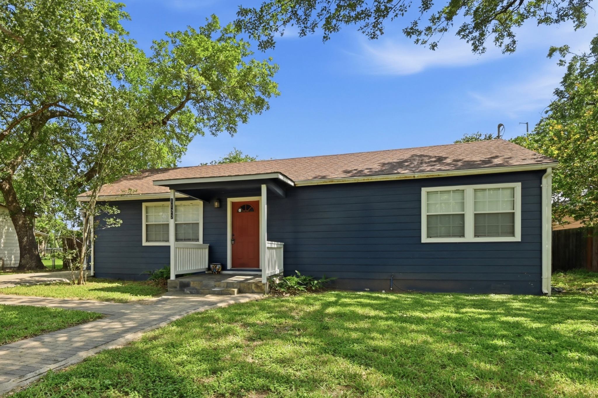 1127 Parr Street Luling, TX 78648 - Photo 2 of 20 A classic facade with rich blue siding and a welcoming red door, surrounded by lush green lawn.
