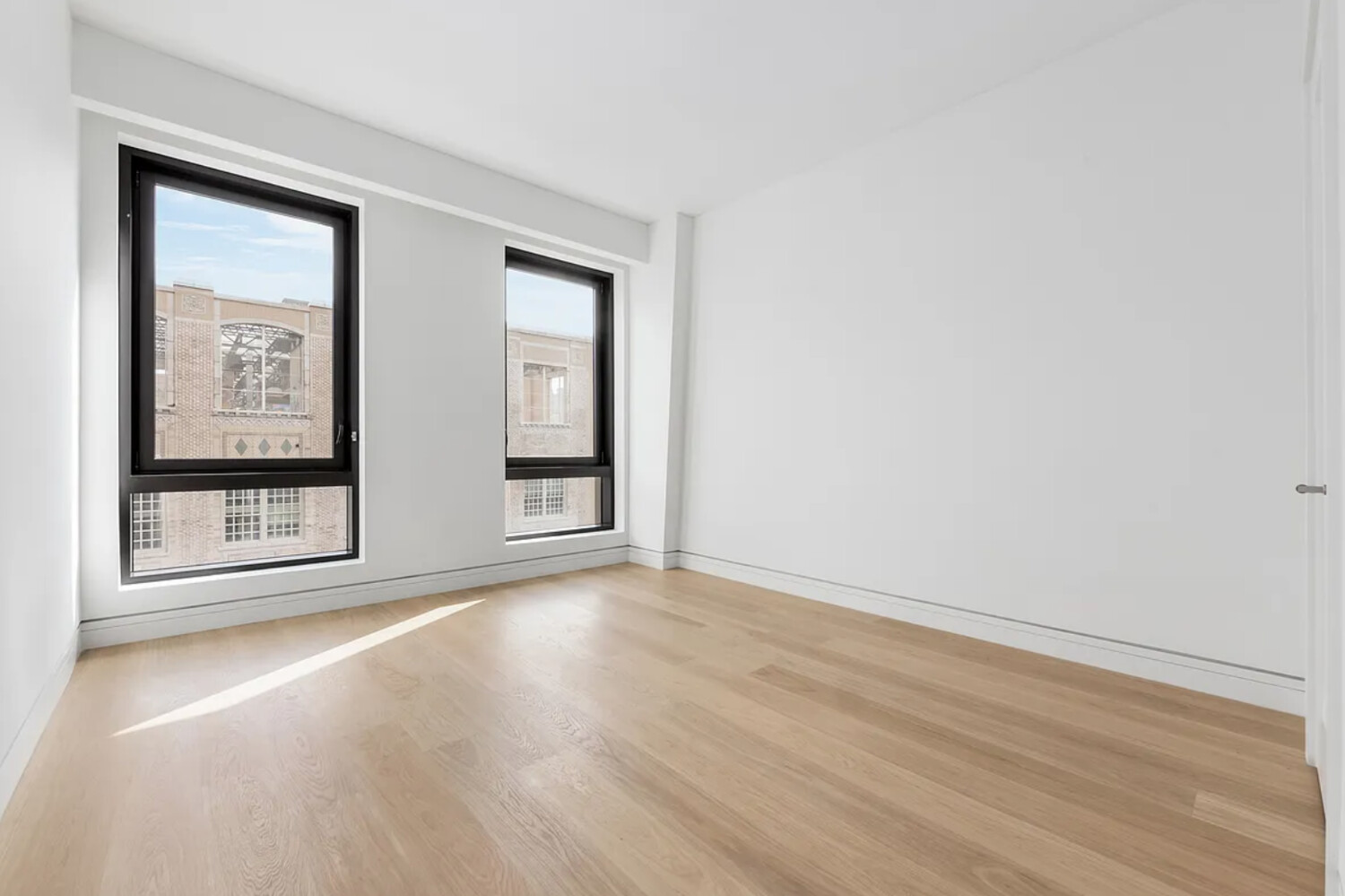 242 Broome Street, Unit 10B Manhattan, NY 10002 - Photo 4 of 10 an empty room with wooden floor and windows