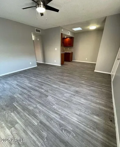 an empty room with wooden floor a ceiling fan a flat screen tv and a potted plant