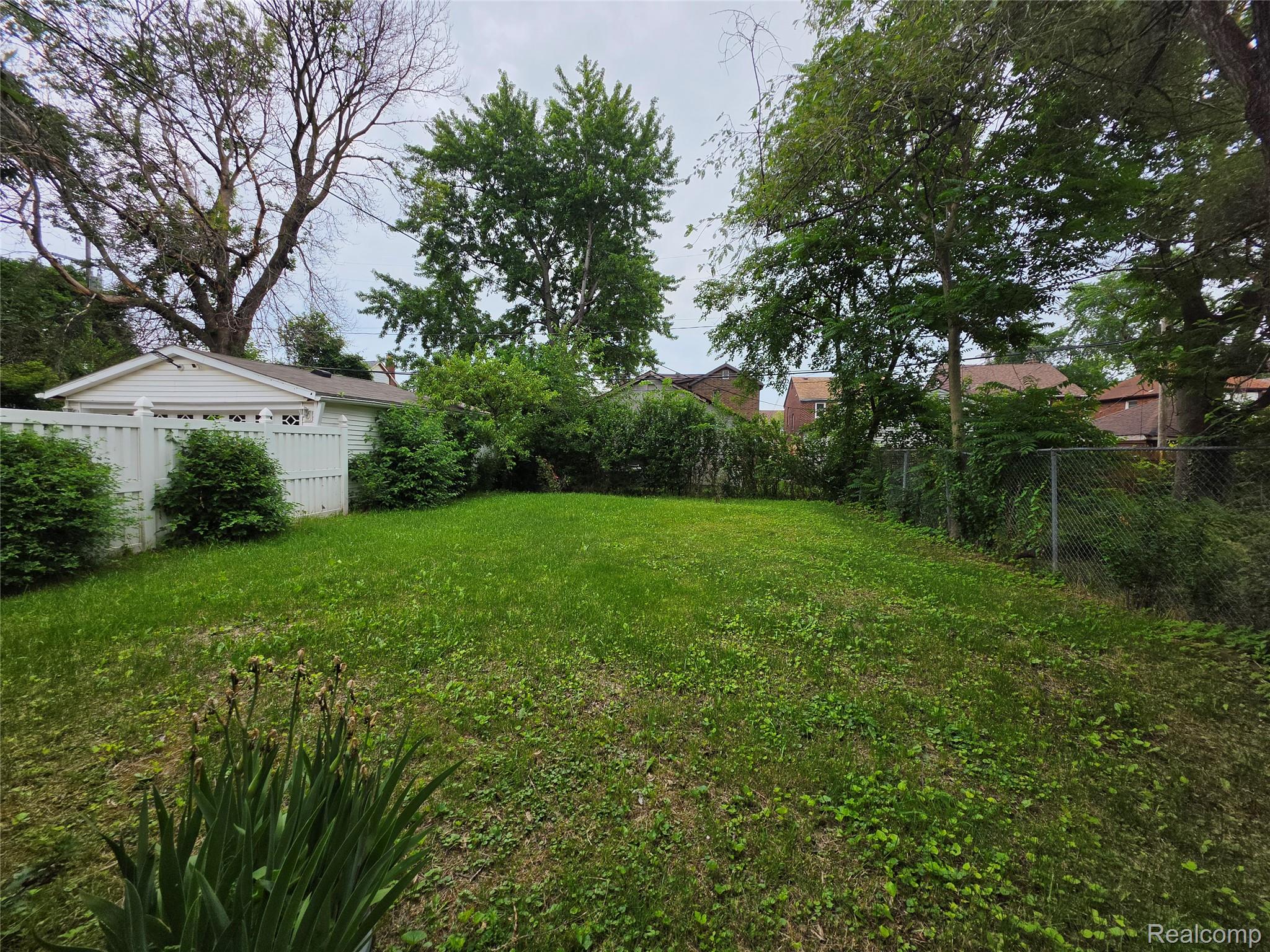15832 Griggs Street Detroit, MI 48238 - Photo 6 of 24 Expansive green space featuring established trees and a combination of white privacy fencing and chain-link fencing