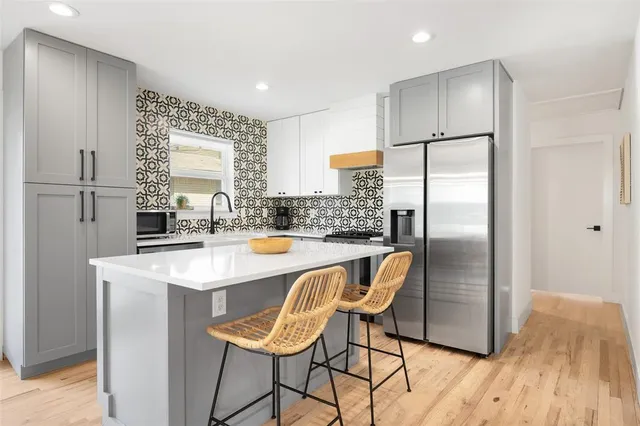 a kitchen with stainless steel appliances granite countertop a refrigerator a sink a stove and white cabinets with wooden floor