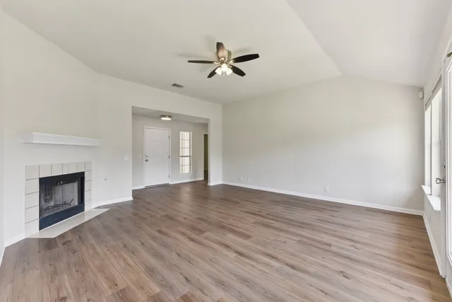 an empty room with wooden floor fireplace and windows