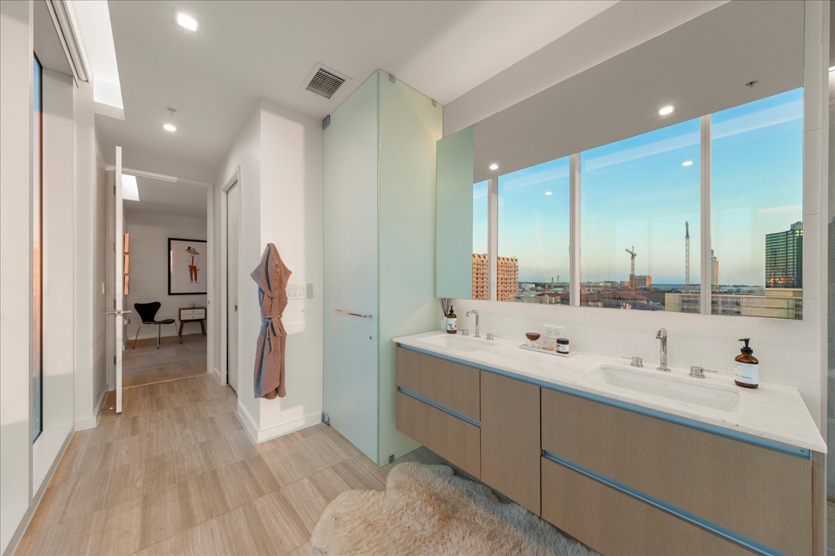 313 West 17th Street, Unit 1104 Austin, TX 78701 - Photo 16 of 40 A serene, light-filled primary bath featuring custom marble counters, a floating double vanity and floor-to-ceiling windows framing sweeping skyline views. Clean lines, natural finishes and thoughtful detailing create a spa-like retreat designed for both daily ease and elevated living.