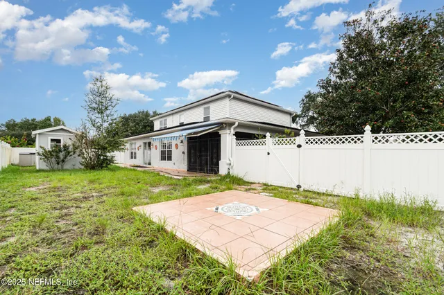 a view of a white house in front of a big yard with plants and large trees