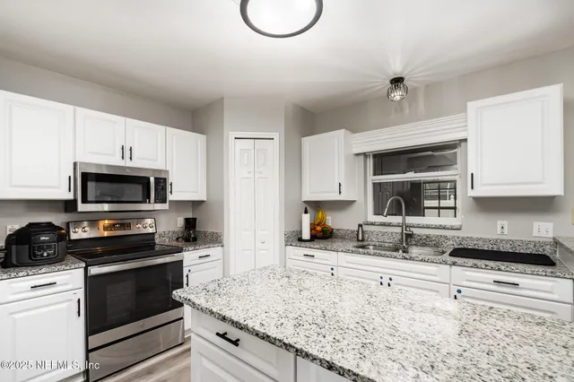 a kitchen with granite countertop a sink a stove top oven a counter space and cabinets