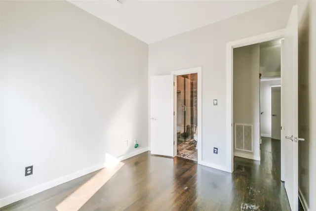 a view of an empty room with wooden floor and a bathroom