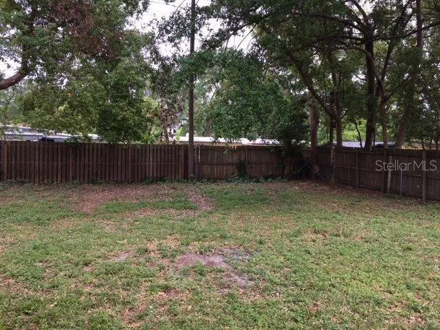 a view of a backyard with large trees and wooden fence