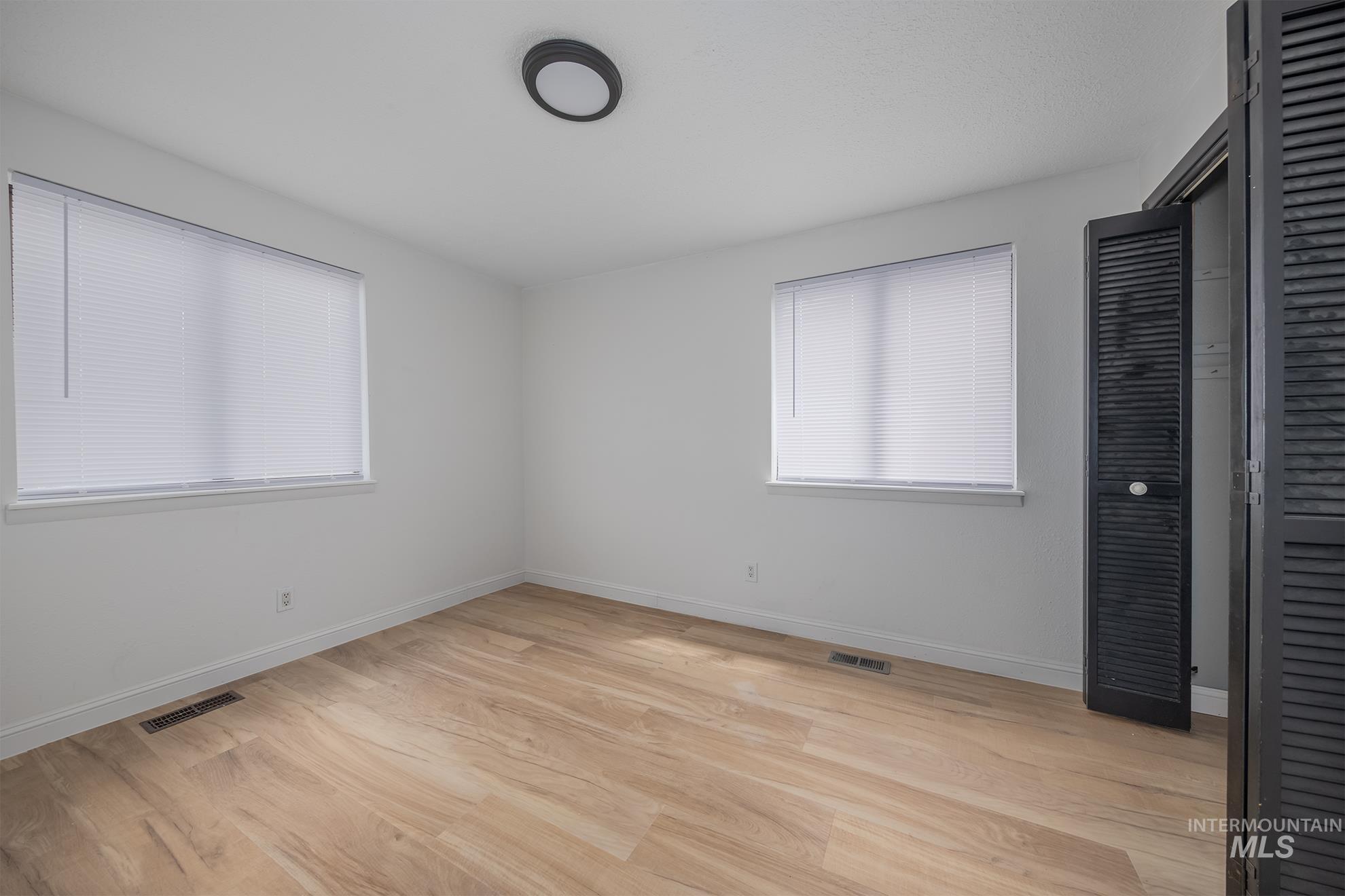 61 Southwest 4th Street Ontario, OR 97914 - Photo 23 of 42 Light wood-finish flooring complements white walls in this room, featuring two windows with white blinds, a black flush-mount ceiling light, and a bi-fold louvered door