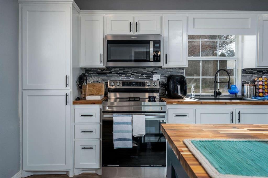 365 Co Road Stamford, TX 79553 - Photo 10 of 23 White shaker-style cabinetry with matte black hardware, stainless steel appliances, mosaic tile backsplash, wood-finish countertops, and an undermount sink with a matte black faucet