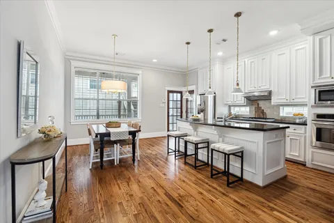 a kitchen with stainless steel appliances granite countertop a stove a refrigerator a kitchen island a dining table and chairs with wooden floor