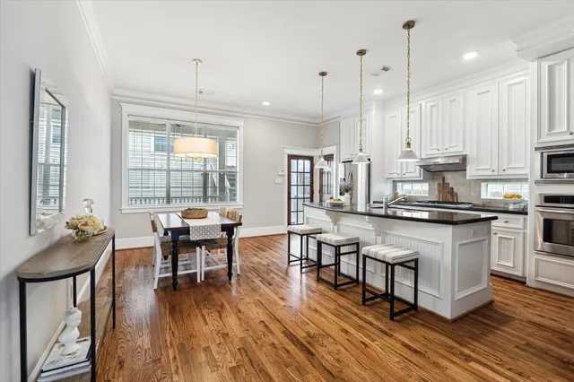 a kitchen with stainless steel appliances granite countertop a stove a refrigerator a kitchen island a dining table and chairs with wooden floor