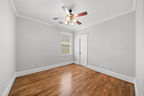 a view of an empty room with wooden floor and a ceiling fan