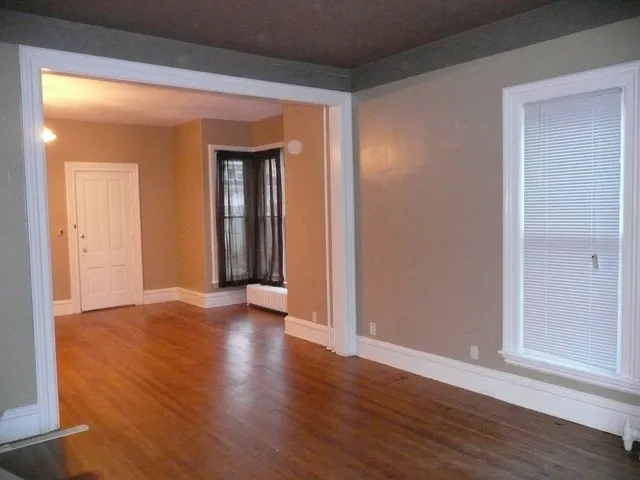 a view of an empty room with wooden floor and a window