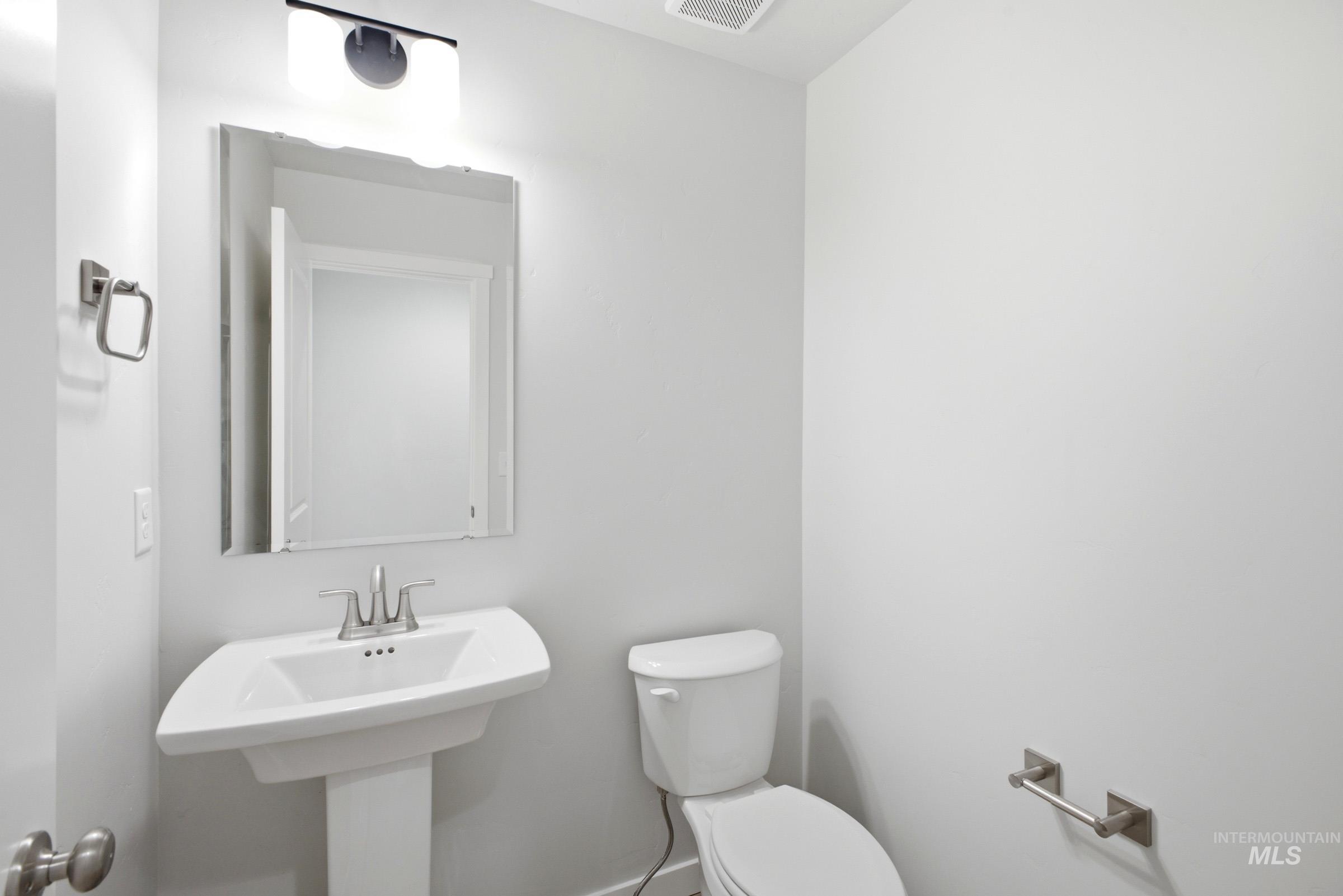 13336 Bank Street Caldwell, ID 83607 - Photo 11 of 24 Pedestal sink with chrome faucet, wall-mounted mirror, overhead vanity lighting, and white toilet