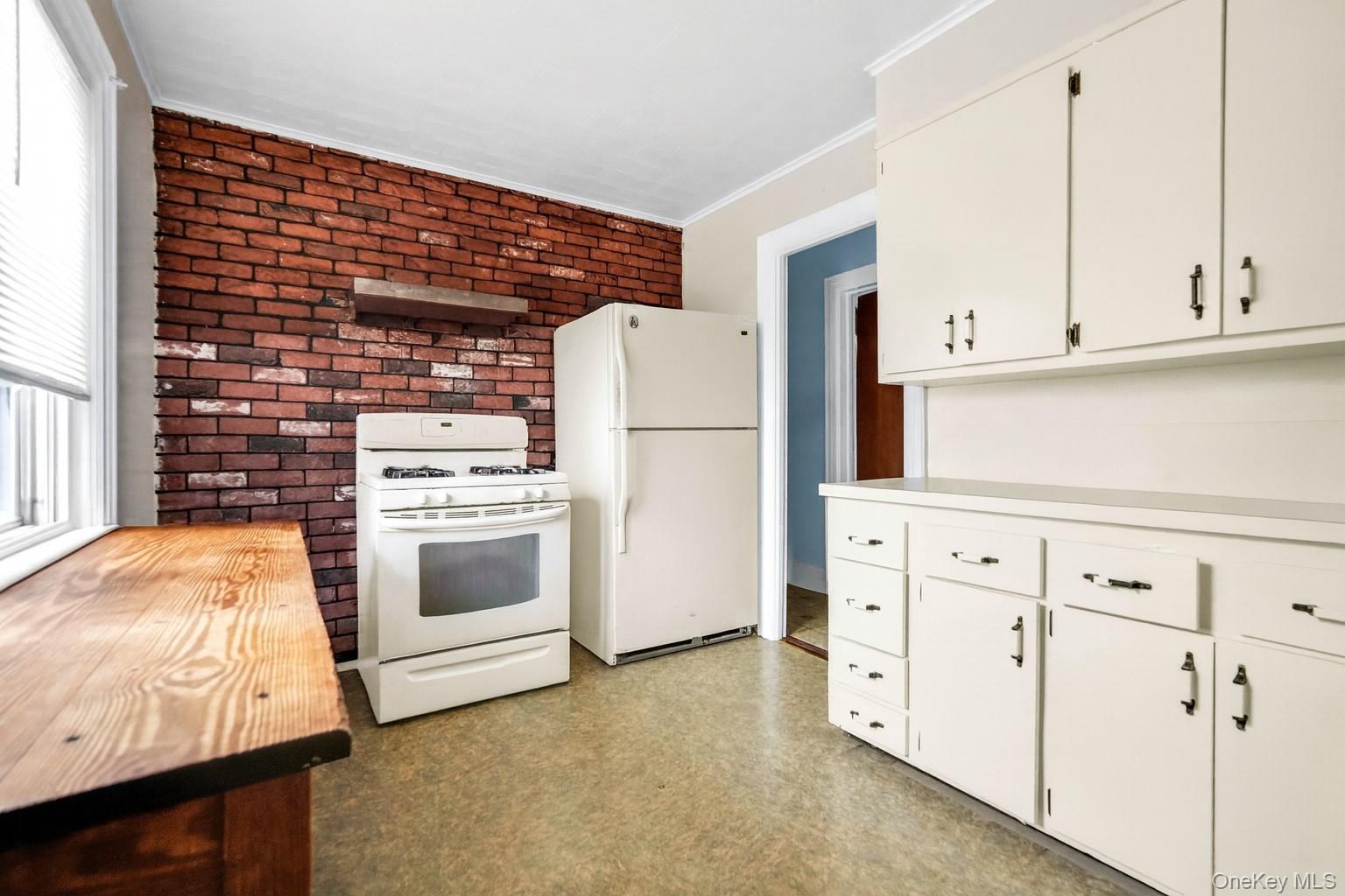 139 Spring Street Ossining, NY 10562 - Photo 13 of 29 Kitchen with white appliances, brick wall, crown molding, white cabinetry, and light floors