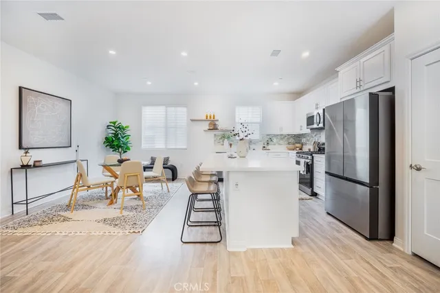 a kitchen with stainless steel appliances kitchen island granite countertop a refrigerator a stove a sink a dining table and chairs with wooden floor