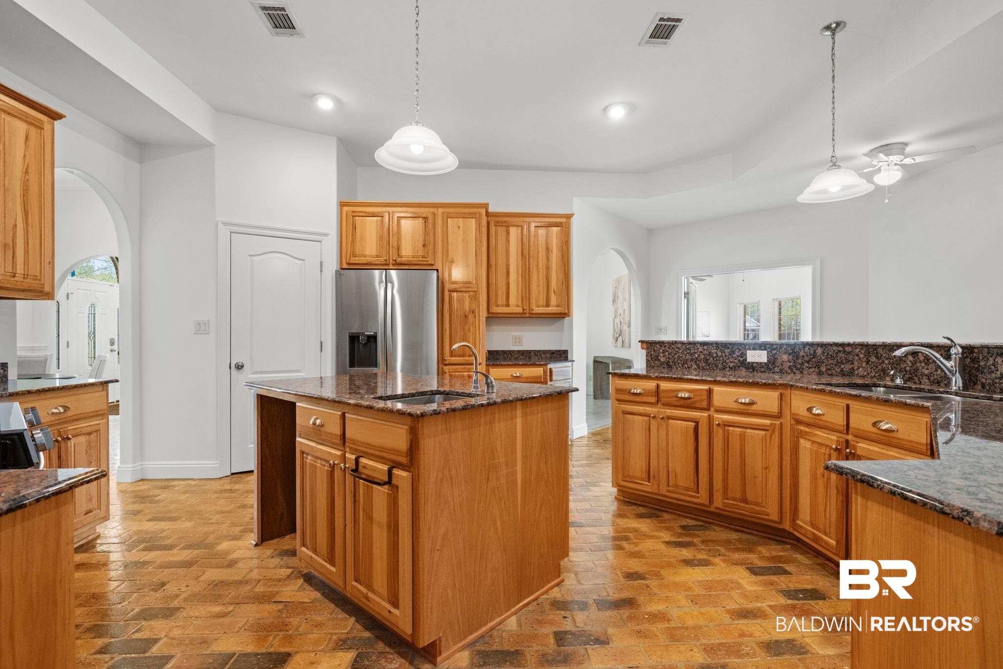 29634 St George Street Daphne, AL 36526 - Photo 22 of 47 Kitchen with arched walkways, dark stone counters, a kitchen island with sink, stainless steel refrigerator with ice dispenser, and wood finish cabinetry