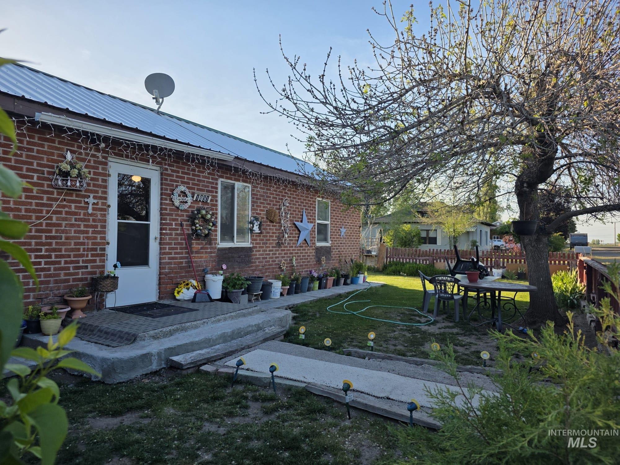 1851 K Street Heyburn, ID 83336 - Photo 1 of 10 Brick exterior featuring a white storm door and window, metal roof, and a mature tree providing shade to the lawn