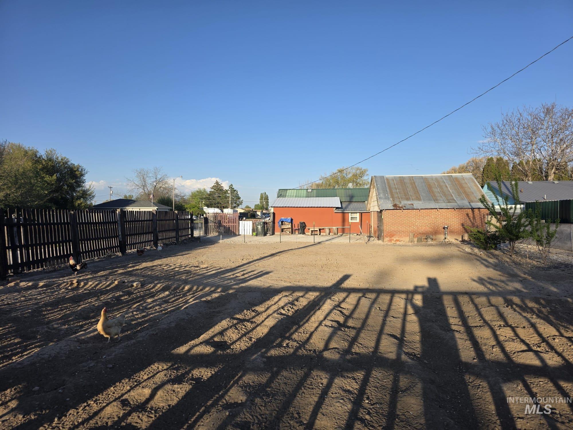 1851 K Street Heyburn, ID 83336 - Photo 10 of 10 Expansive gravel lot with a dark-stained wooden fence and a brick-built structure featuring a corrugated metal roof