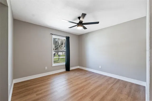 an empty room with wooden floor fan and windows