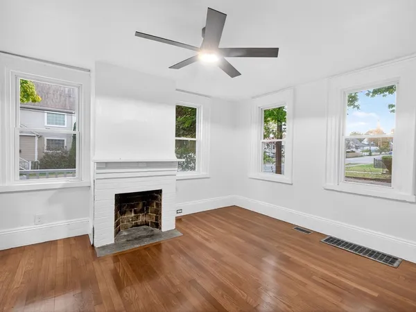 a view of an empty room with wooden floor fireplace and a window