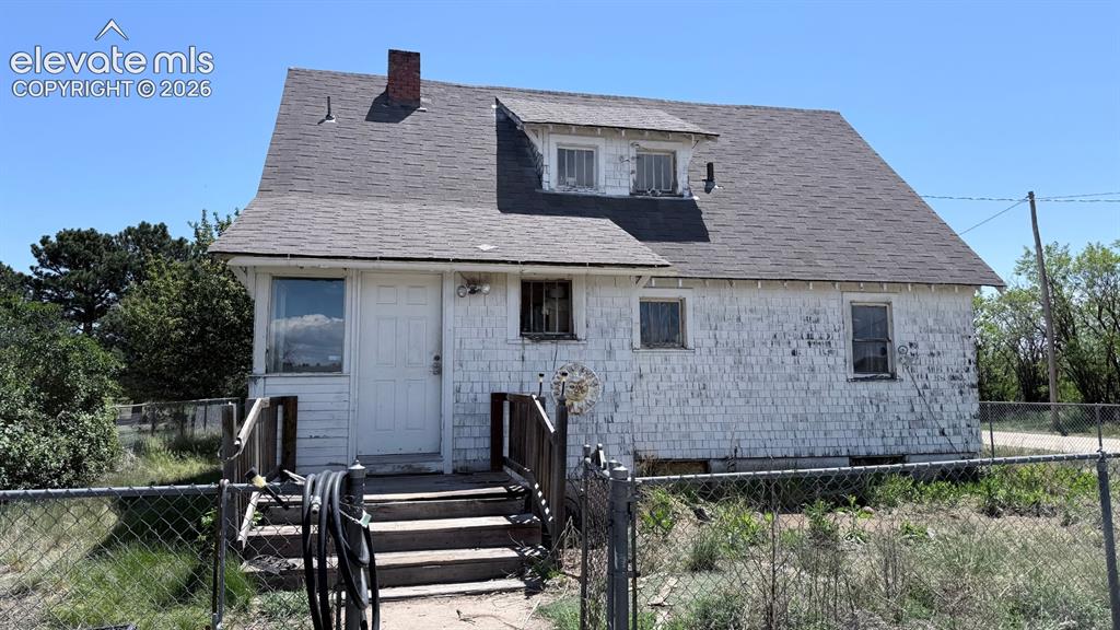 3380 Curtis Road Peyton, CO 80831 - Photo 12 of 13 Two-story residential structure with white shingle siding, a gray shingle roof, and a red brick chimney