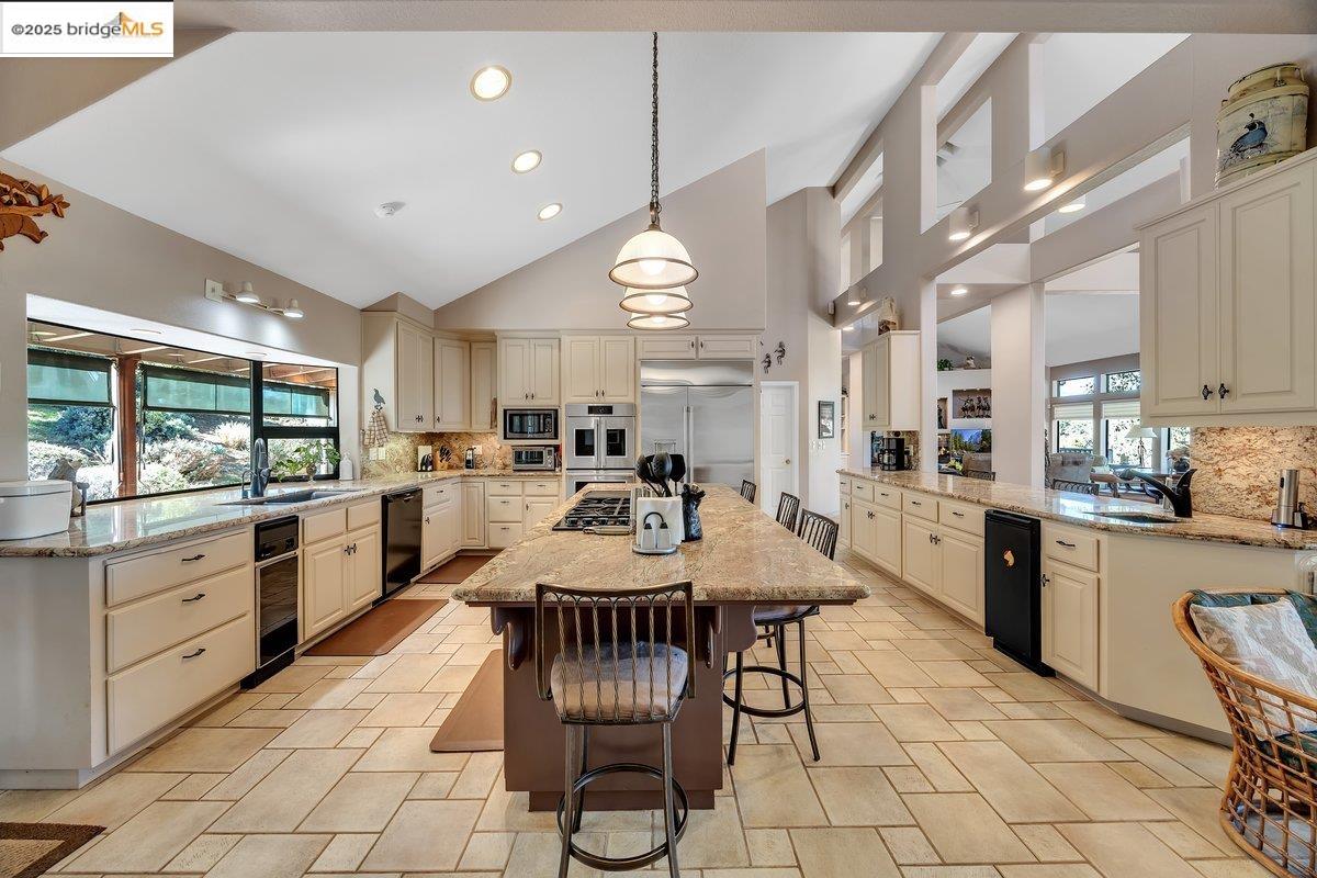 13700 Clements Road Groveland, CA 95321 - Photo 14 of 93 Kitchen with decorative backsplash, light stone countertops, high vaulted ceiling, a center island, and decorative light fixtures