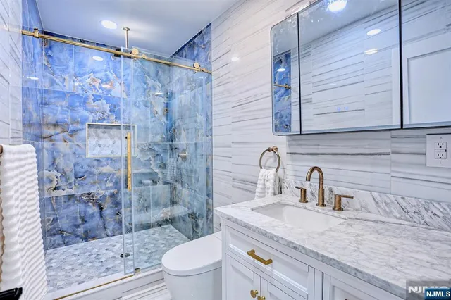 a bathroom with a granite countertop sink a toilet a mirror and shower