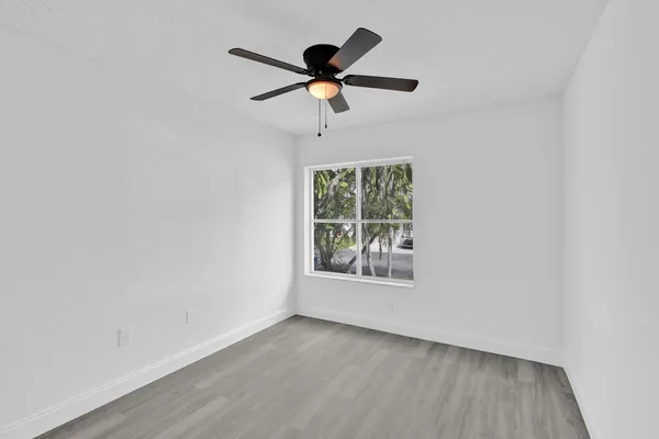 an empty room with wooden floor ceiling fan and windows