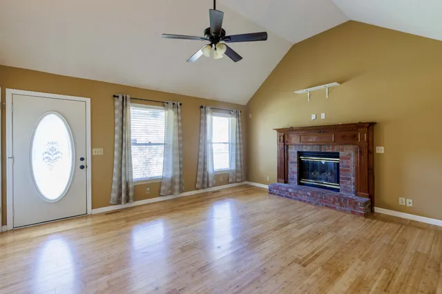 an empty room with wooden floor fireplace and windows
