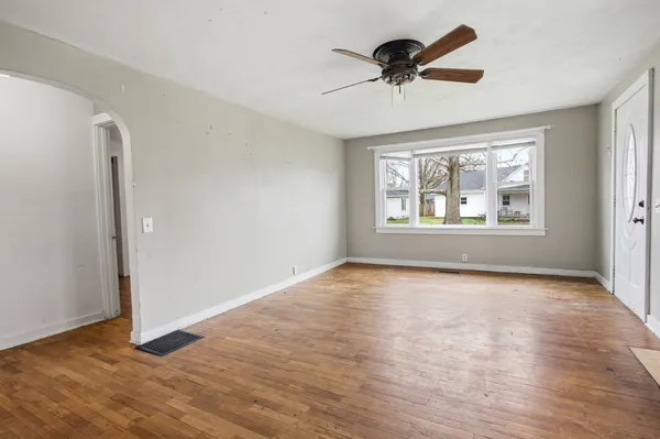 an empty room with wooden floor chandelier fan and windows