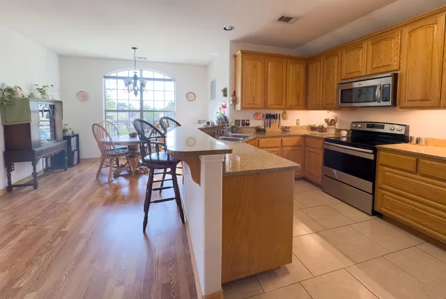 a kitchen with stainless steel appliances granite countertop wooden floor a stove top oven a sink dishwasher a dining table and chairs with wooden floor