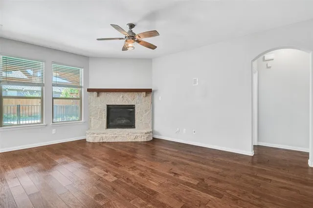 an empty room with wooden floor a ceiling fan and windows