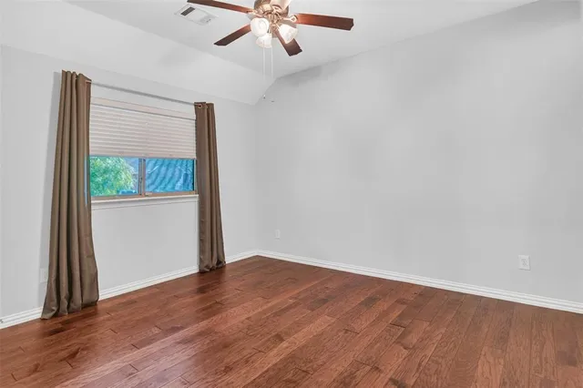 an empty room with wooden floor fan and windows