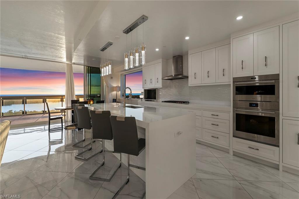 13945 Old Coast Road, Unit 806 Naples, FL 34110 - Photo 32 of 50 a kitchen with stainless steel appliances kitchen island granite countertop a stove top oven a sink a dining table and chairs with the cabinets