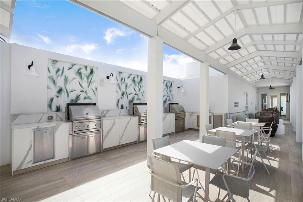 13945 Old Coast Road, Unit 806 Naples, FL 34110 - Photo 38 of 50 a kitchen with stainless steel appliances kitchen island granite countertop a refrigerator a stove a sink a dining table and chairs with wooden floor