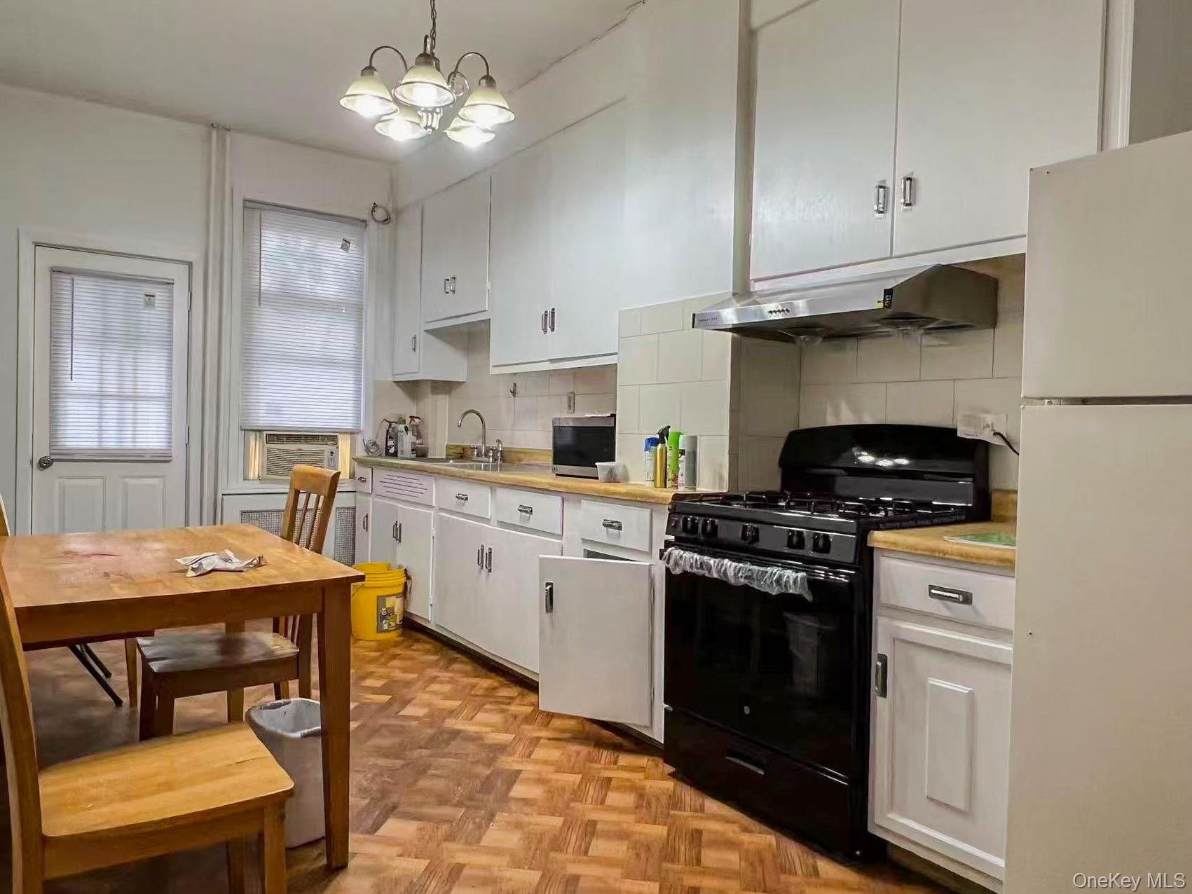 22-32 124th Street Queens, NY 11356 - Photo 2 of 8 Kitchen featuring gas stove, freestanding refrigerator, backsplash, white cabinetry, and ventilation hood