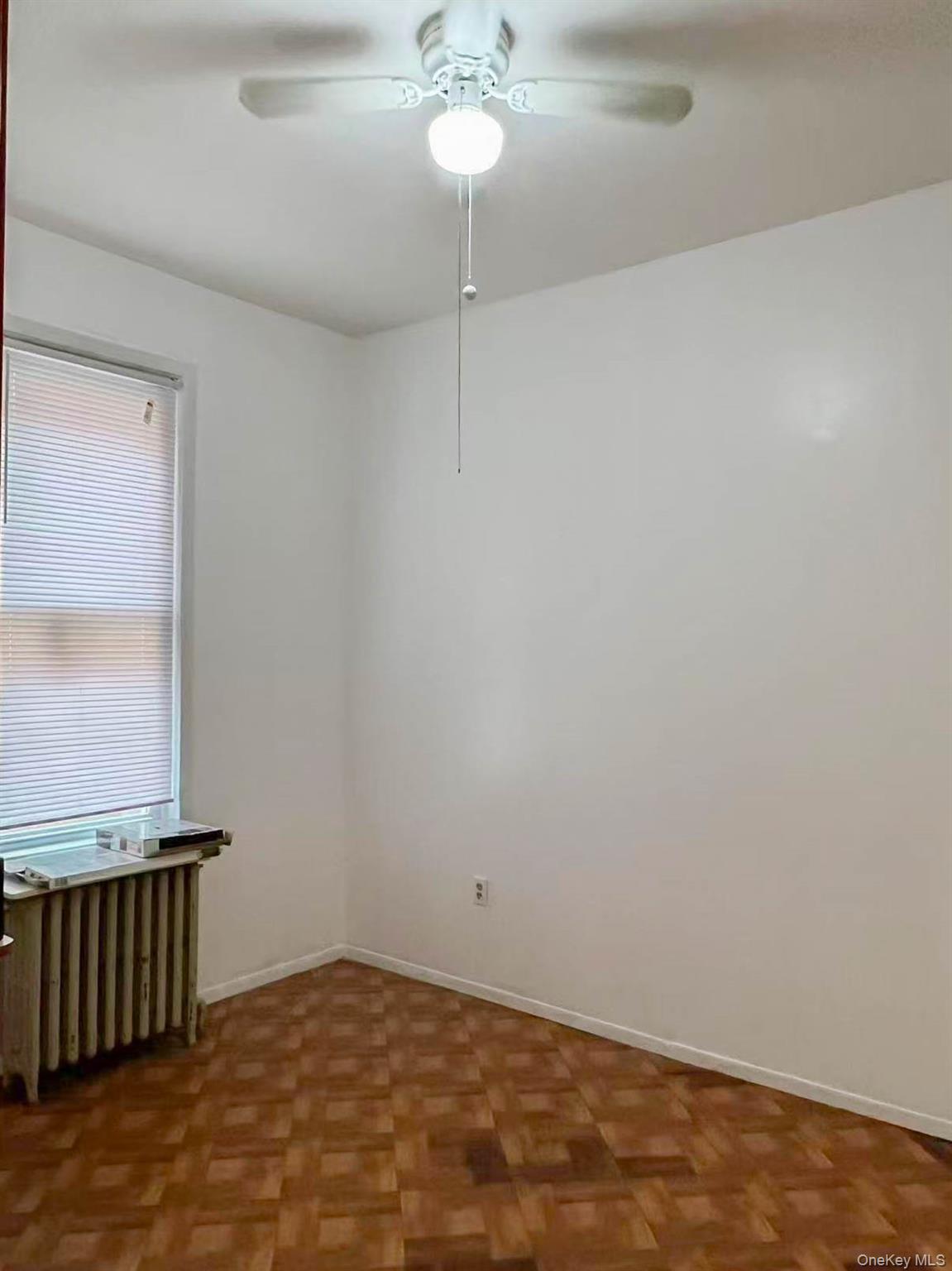 22-32 124th Street Queens, NY 11356 - Photo 4 of 8 Empty room featuring radiator heating unit and ceiling fan