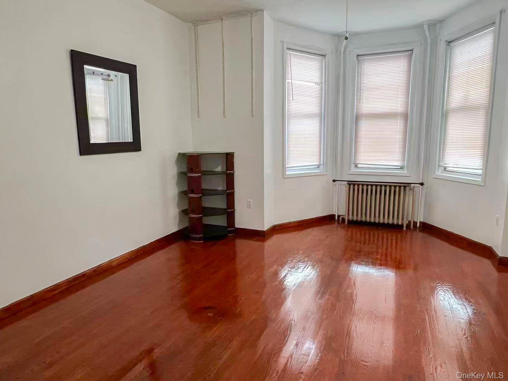 22-32 124th Street Queens, NY 11356 - Photo 5 of 8 Spare room featuring dark wood-style flooring, radiator, and healthy amount of natural light