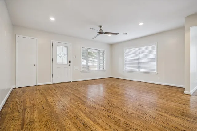 an empty room with wooden floor ceiling fan and windows
