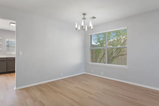 an empty room with wooden floor chandelier and windows