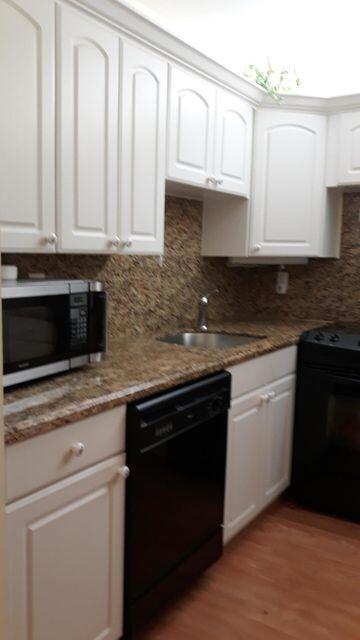 9355 Southwest 8th Street, Unit 121 Boca Raton, FL 33428 - Photo 8 of 35 a kitchen with granite countertop white cabinets and black appliances