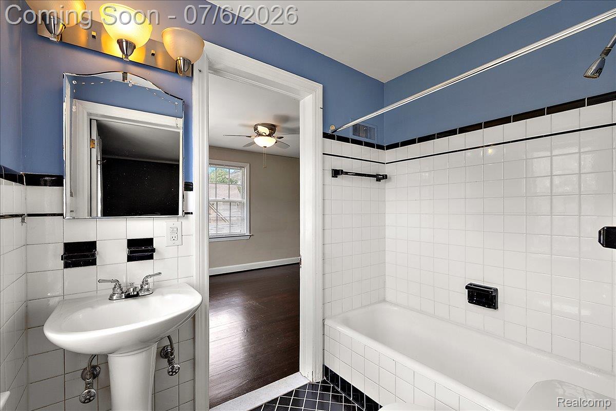1051 Devonshire Road Grosse Pointe, MI 48230 - Photo 48 of 98 Bathroom featuring white square wall tiles with black accent tiles and trim, a pedestal sink with chrome fixtures, a full bathtub with shower, and a vanity light fixture