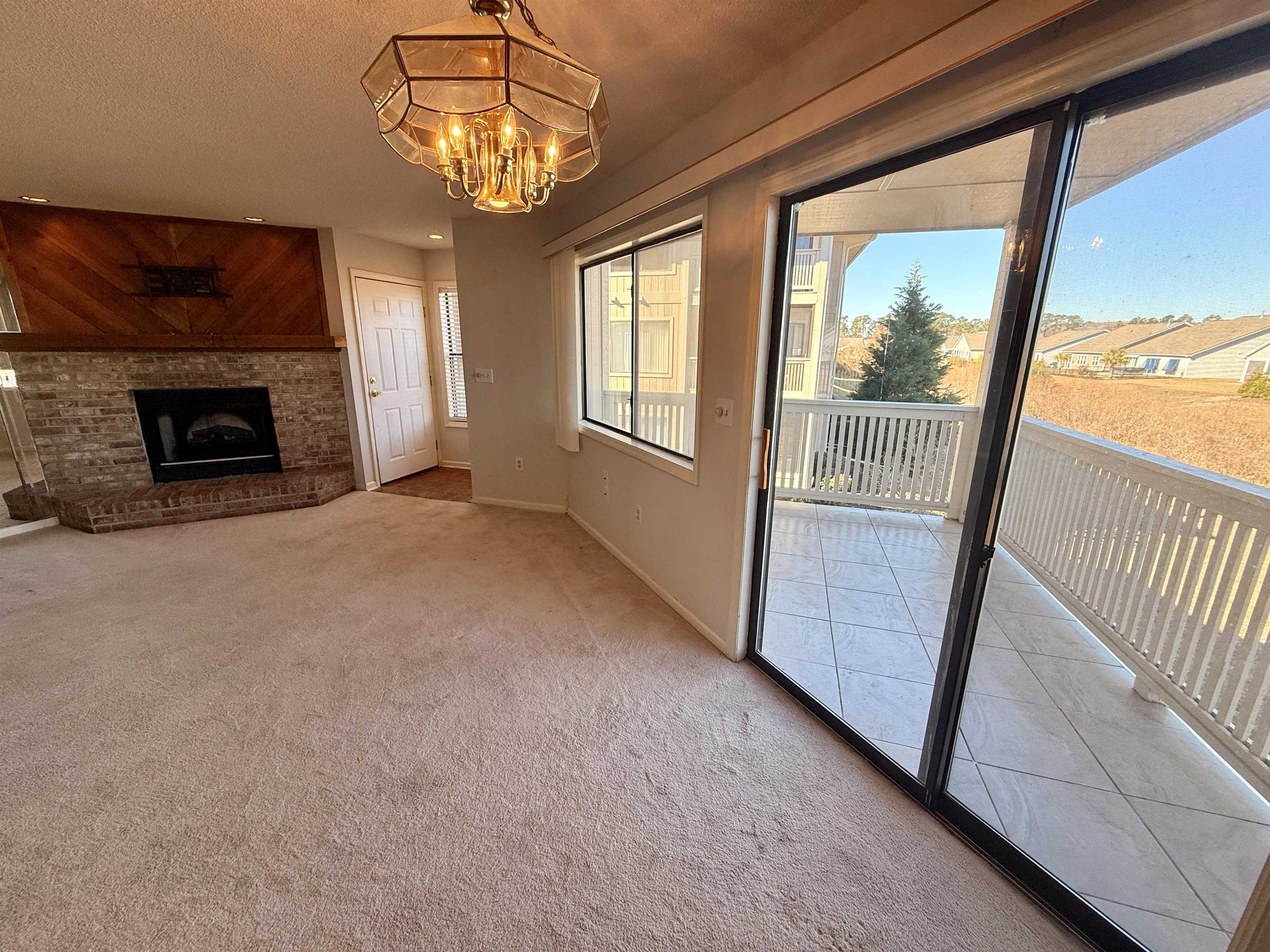 4230 Pinehurst Circle, Unit K4 Little River, SC 29566 - Photo 4 of 25 Unfurnished living room with light carpet, a fireplace, a textured ceiling, and a chandelier